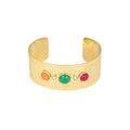 A wide gold cuff bracelet featuring five colorful round cabochon stones set across the front, displayed on a clean white background.