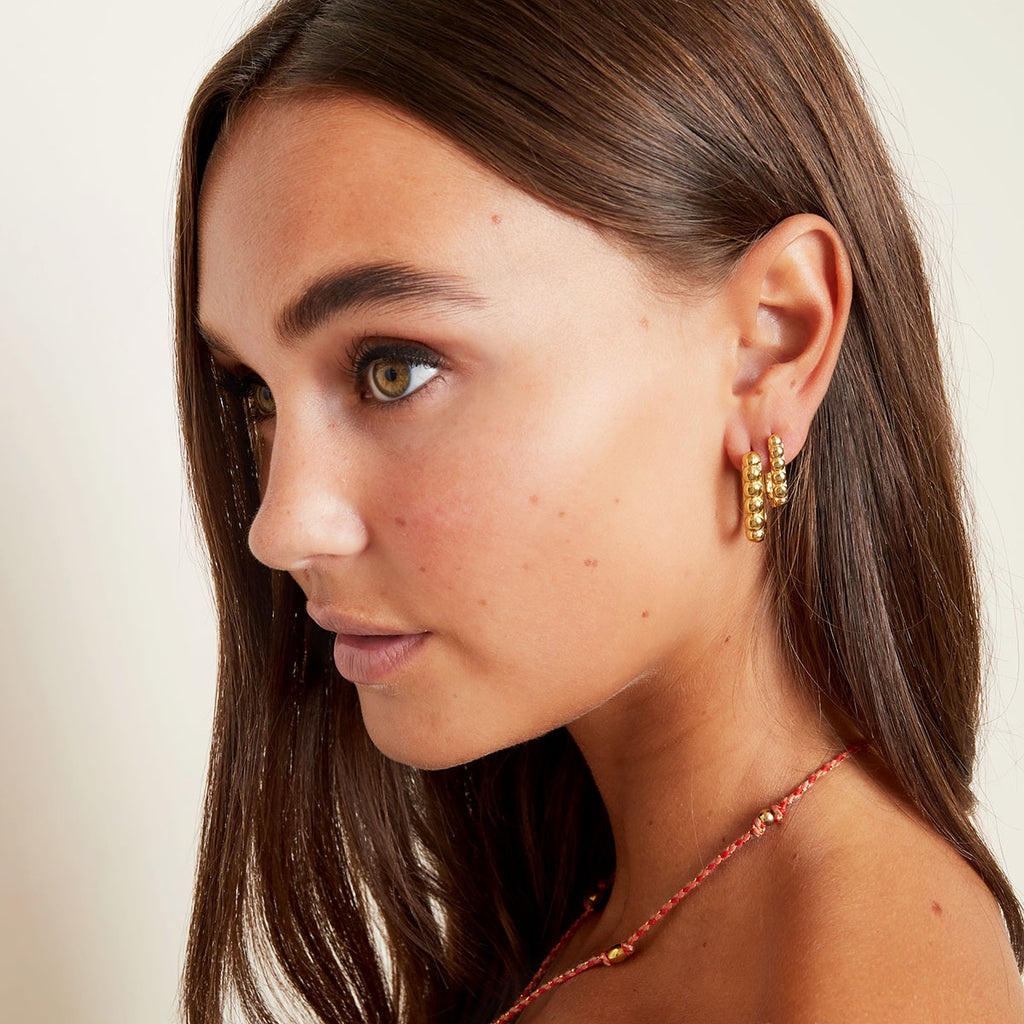 Close-up of a woman wearing gold earrings with a neutral background